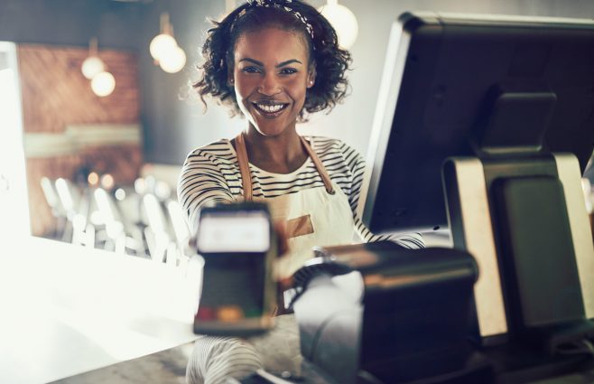 Smiling young bistro waitress holding an electronic card payment machine